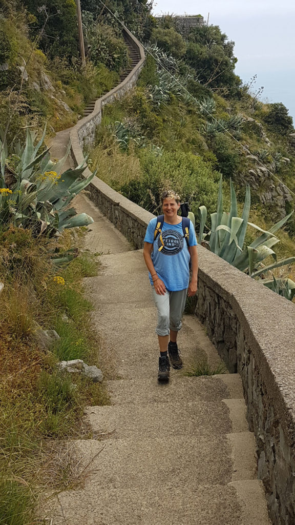 Eine Frau mit kurzen, dunklen Haaren in Wanderschuhen steigt einen Treppenpfad hinauf. Beim Wandern an der Amalfiküste kommt man ums Treppensteigen nicht herum.